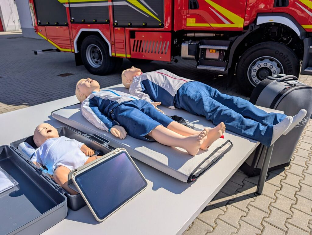 Manekin z manekinem na stole obok wozu strażackiego.