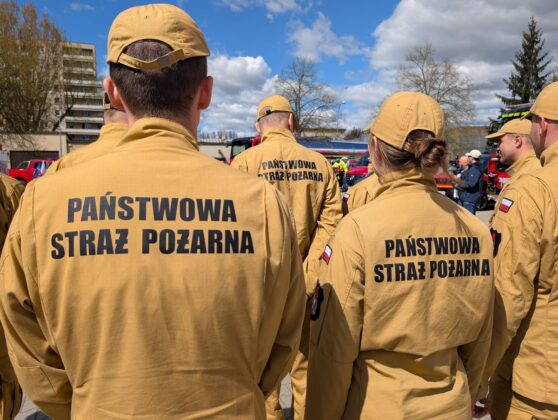 Grupa ludzi w mundurach z napisem "państwowa straż pożarna" na tle neutralnego tła.