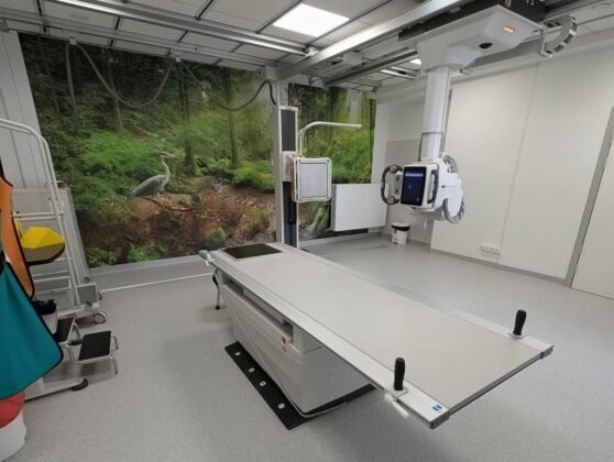 Szpitalny pok&oacute;j z dużym stołem medycznym, otoczony sprzętem medycznym i neutralnymi ścianami.