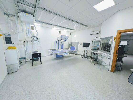 Pok&oacute;j szpitalny z ł&oacute;żkiem, fotelem i innym wyposażeniem medycznym.