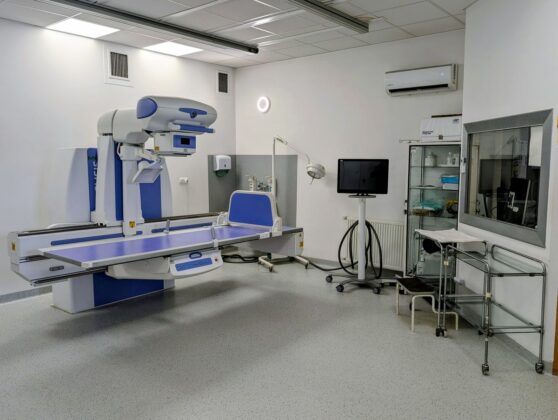 Szpitalny pok&oacute;j z dużym sprzętem medycznym, w tle widoczne ł&oacute;żko pacjenta i okno z naturalnym światłem.