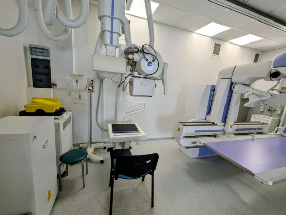 Medyczny pok&oacute;j z stołem, krzesłem i r&oacute;żnym sprzętem medycznym.