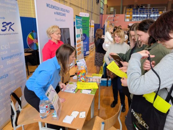 Ludzie stoją wok&oacute;ł stołu z widocznym znakiem na nim.