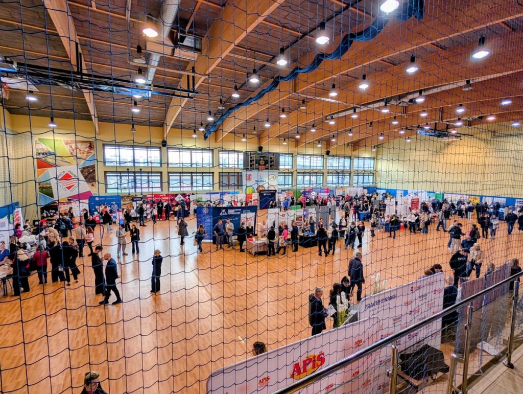 Wnętrze dużej siłowni z osobami poruszającymi się w różnych kierunkach.