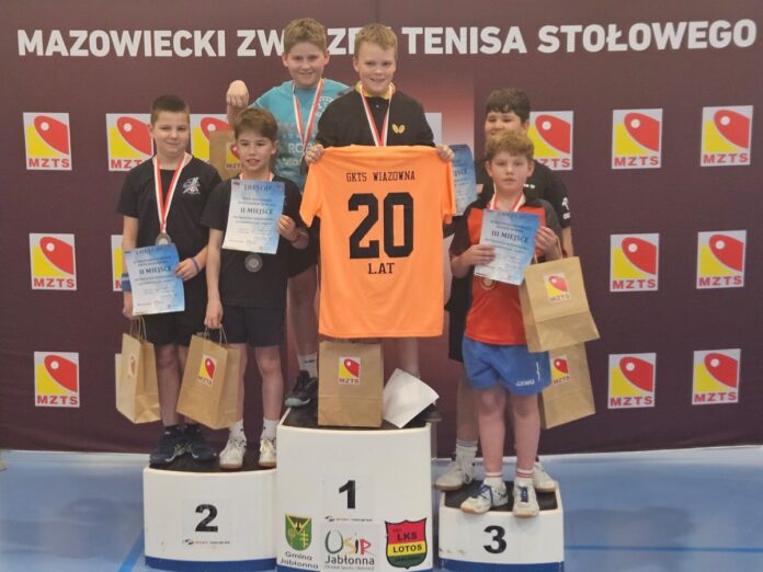 Grupa młodych chłopców na podium trzymających swoje trofea z uśmiechami na twarzach.