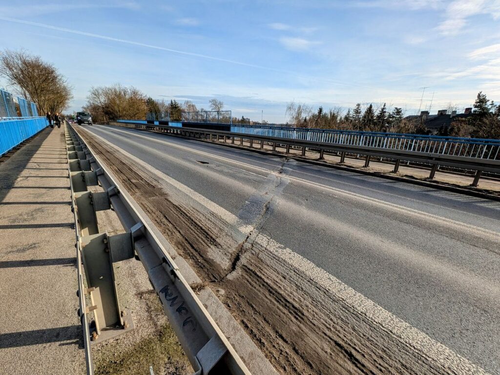 Ulica z popękaną nawierzchnią, barierki po obu stronach wskazują na to, że jest to wiadukt. 
