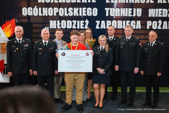 Grupa ludzi stoi przed dużym banerem, uśmiechając się i pozując do zdjęcia.