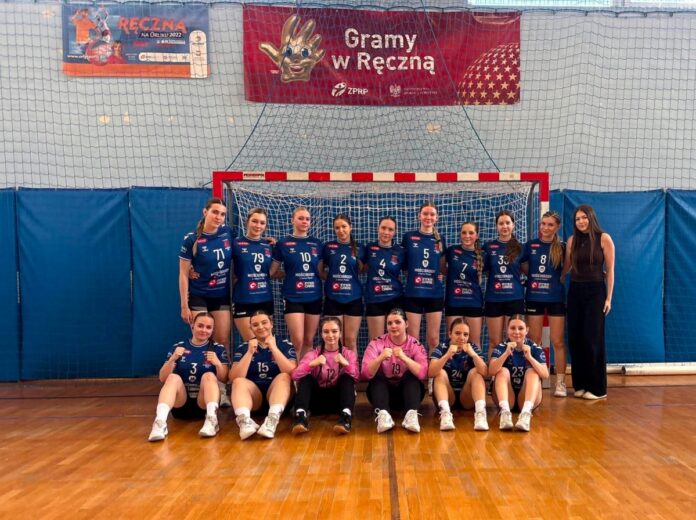 Zespół siatkarek pozujący do zdjęcia w strojach sportowych na boisku.