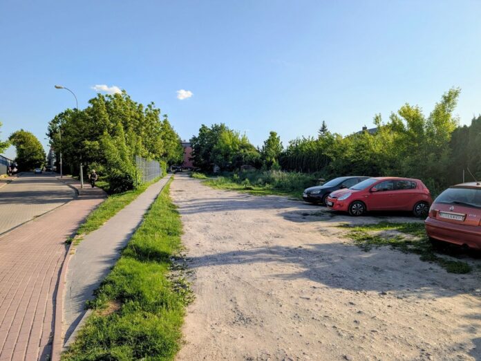 Działka z dzikimi krzewami będąca dzikim parkingiem z kilkoma samochodami.