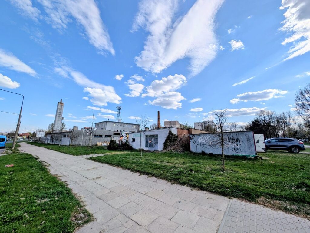 Widok na stare niewysokie budynki poprzemysłowe stojące przy chodniku.