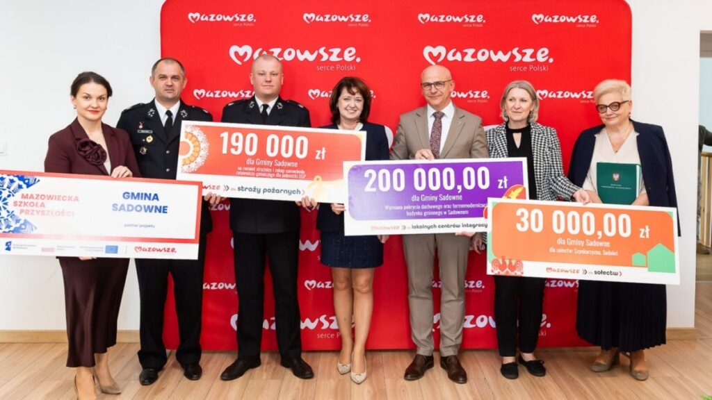 Grupa ludzi trzymająca duże czeki, uśmiechając się i celebrując osiągnięcia finansowe.