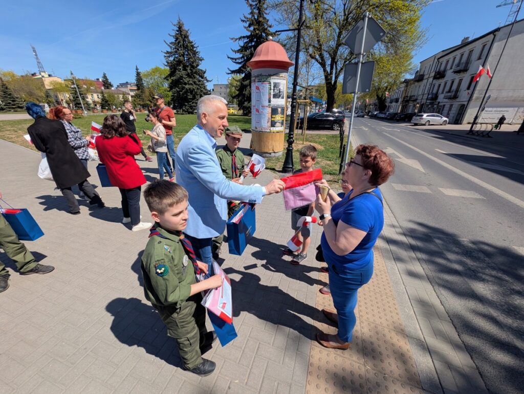 Mężczyzna rozdaje dzieciom czerwone flagi na ulicy.