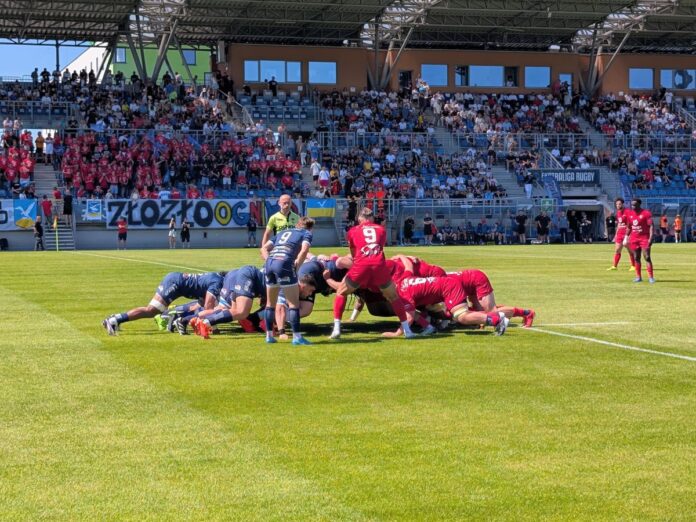 Zawodnicy w niebieskich i czerwonych strojach formują młyn podczas meczu rugby na stadionie