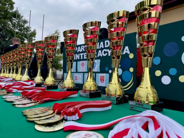 Stół z wieloma trofeami i medalami, prezentującymi osiągnięcia i nagrody.