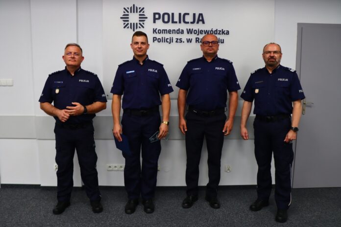 Policjanci w mundurach pozują na tle znaku, prezentując się w radosnej atmosferze.
