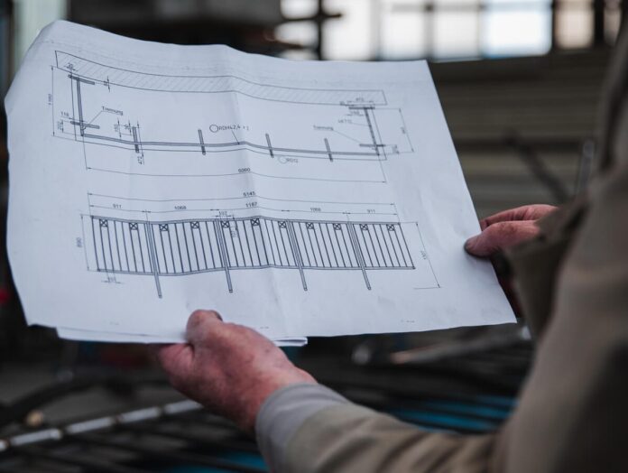 Mężczyzna trzymający w ręku plan architektoniczny, skupiony na szczegółach projektu.