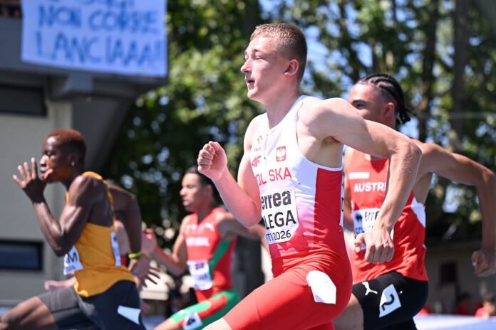 Polski sprinter w biało-czerwonym stroju biegnie w wyścigu obok innych lekkoatletów