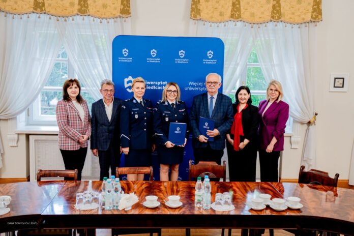 Przedstawiciele Uniwersytetu w Siedlcach oraz policji pozują do wspólnego zdjęcia z teczkami na tle logo uczelni