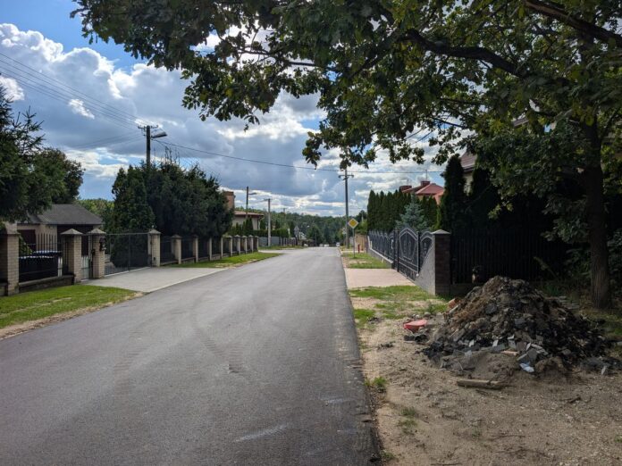 Asfaltowa ulica wśród domów jednorodzinnych ze stertą ziemi i gruzu na poboczu