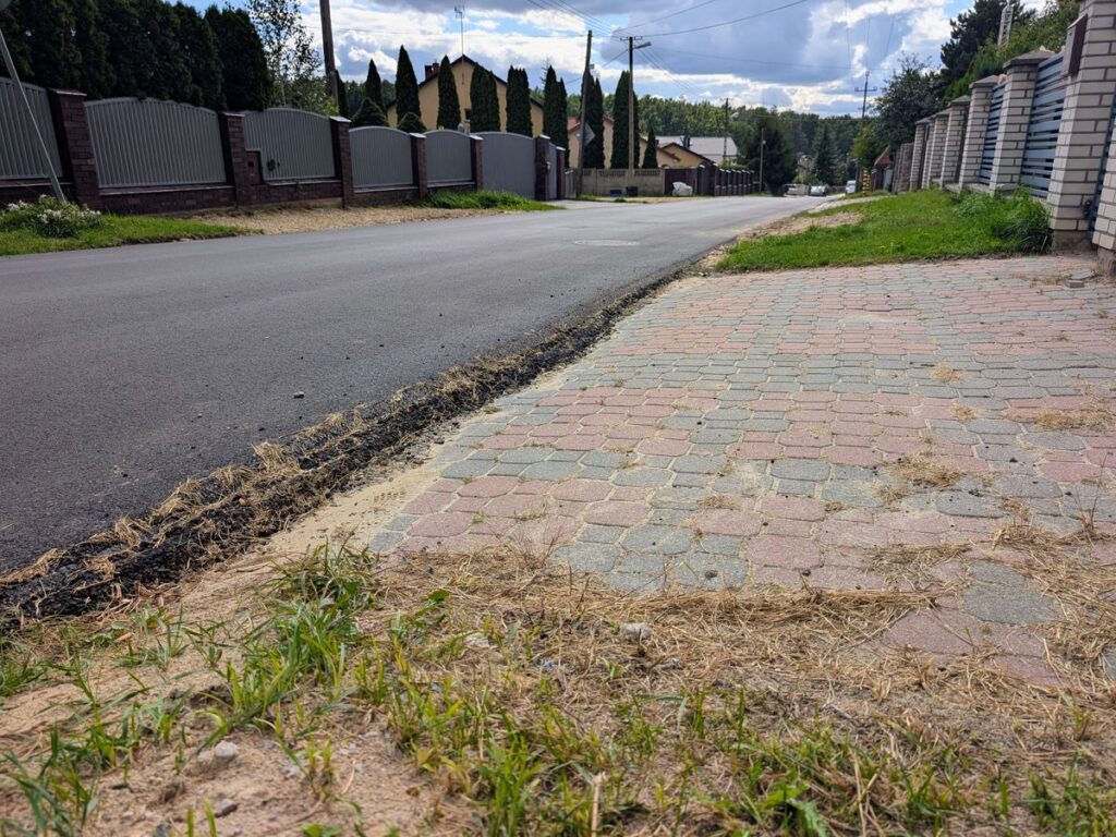 Nowo wyasfaltowana droga z chodnikiem z kostki brukowej na osiedlu domów jednorodzinnych