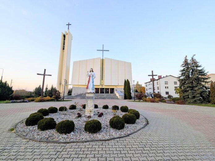 Figura Jezusa Miłosiernego na placu przed nowoczesnym kościołem z wysoką dzwonnicą