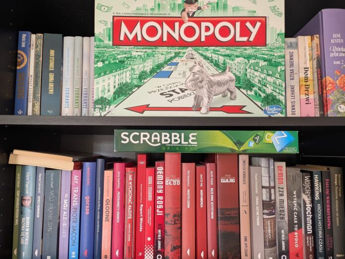 Półki z książkami, na których umieszczono pudełka gier planszowych Monopoly i Scrabble