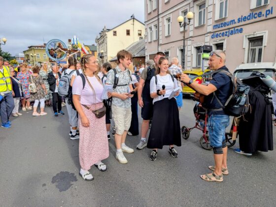 Młodzi ludzie z mikrofonami i mężczyzna z gitarą śpiewający na ulicy podczas Pieszej Pielgrzymki Podlaskiej