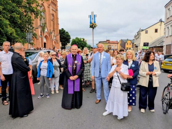 Biskup w fioletowej stule i grupa os&oacute;b przed ceglanym kościołem podczas wydarzenia religijnego