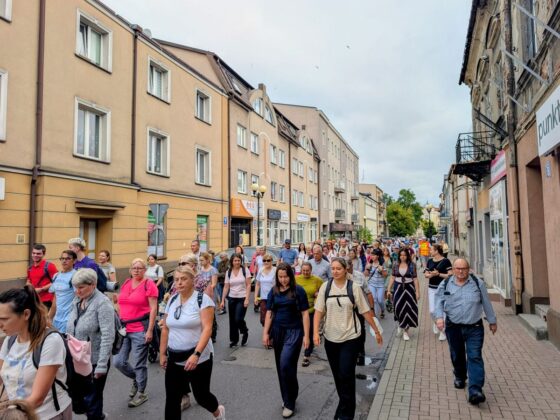 Duża grupa ludzi idąca ulicą miasta między kamienicami