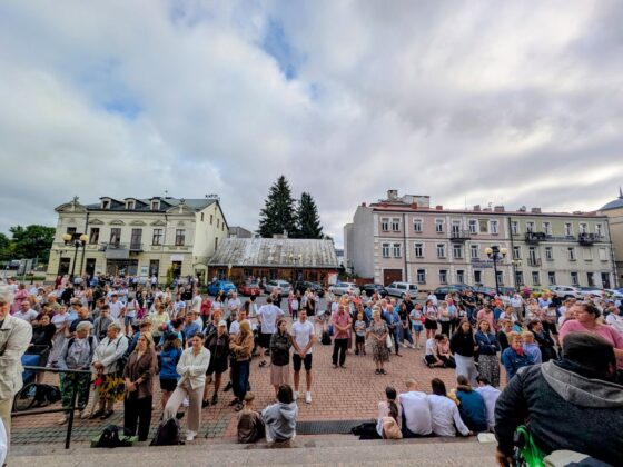 Tłum ludzi zgromadzony na placu przed kościołem pod zachmurzonym niebem
