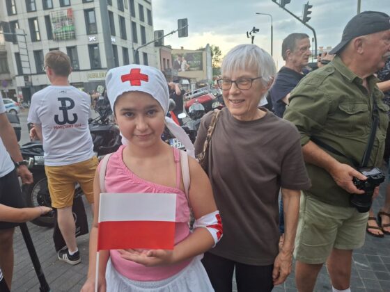 Dziewczynka w stroju sanitariuszki z polską flagą i starsza kobieta podczas obchod&oacute;w rocznicy Powstania Warszawskiego