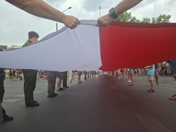 Ludzie trzymający wielką biało-czerwoną flagę Polski rozciągniętą nad ulicą podczas uroczystości