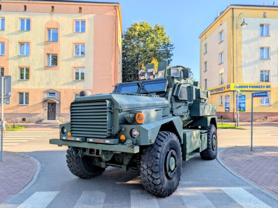 Opancerzony pojazd wojskowy zaparkowany na miejskiej ulicy w otoczeniu budynk&oacute;w mieszkalnych