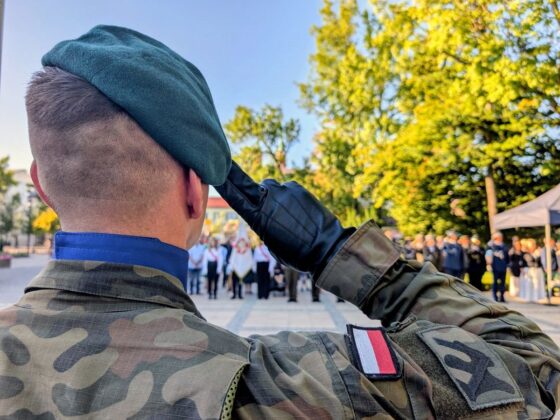 Żołnierz w polskim mundurze i zielonym berecie salutuje podczas uroczystości