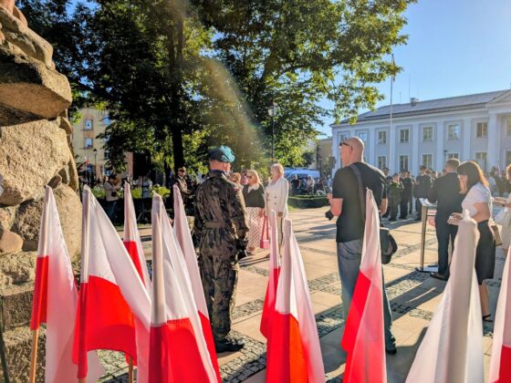 Żołnierz na baczność i polskie flagi podczas uroczystości patriotycznej na placu miejskim