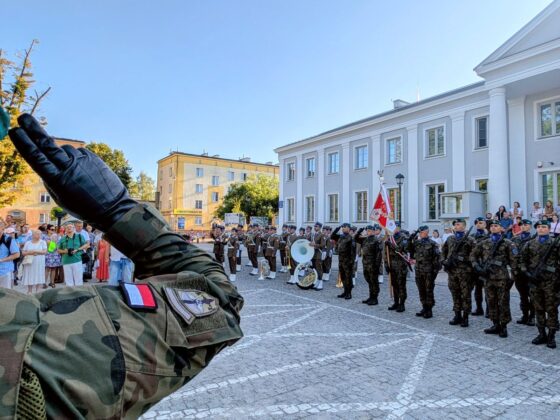 Żołnierz salutuje przed formacją wojskową i orkiestrą dętą podczas uroczystości na placu miejskim