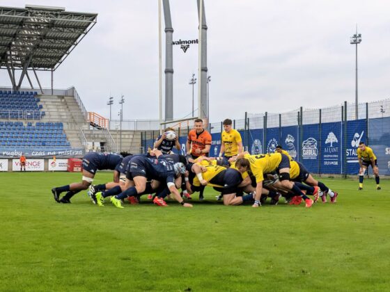 Zawodnicy w granatowych i ż&oacute;łtych strojach formują młyn podczas meczu rugby na boisku