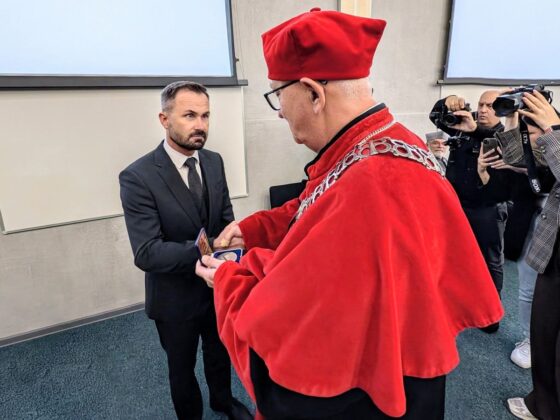 Rektor w czerwonej todze i birecie wręcza medal mężczyźnie w garniturze