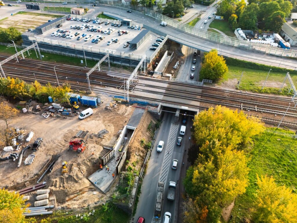 Widok z lotu ptaka na plac budowy przejazdu pod torami kolejowymi i pobliski parking samochodowy